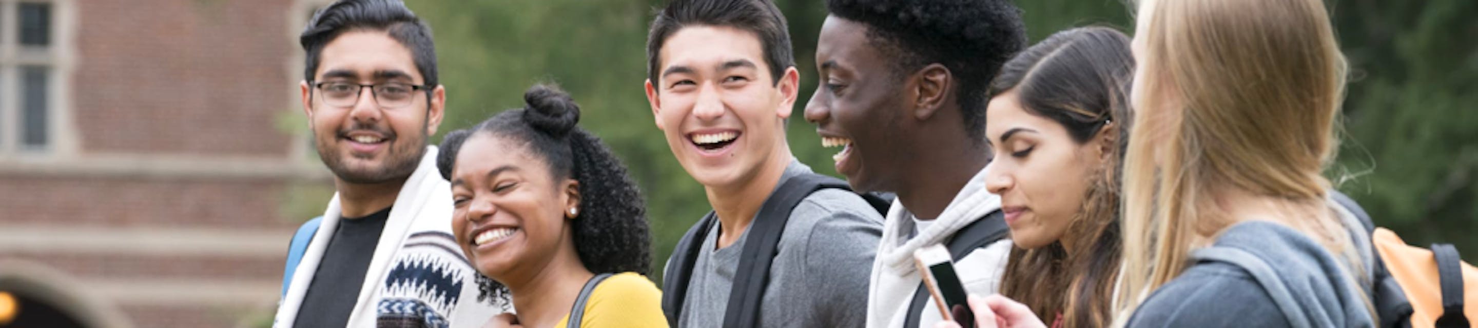 six young adults with backpacks and phones walk forward smiling and laughing