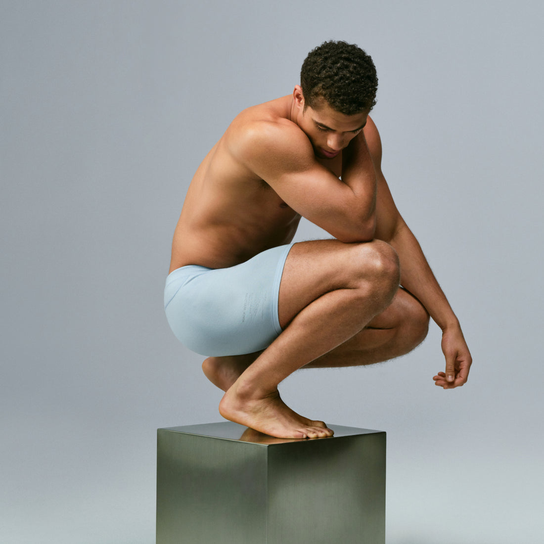 man wearing SILVER boxer briefs perches on a silver cube