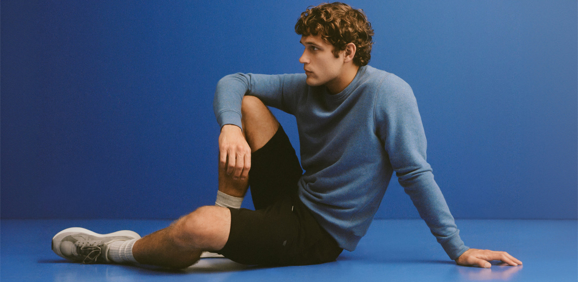 Man sitting on the ground in a long sleeve baby blue sweater and shorts