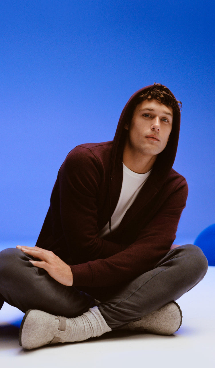 Image of a man in a zip up hoodie sitting criss cross on the floor