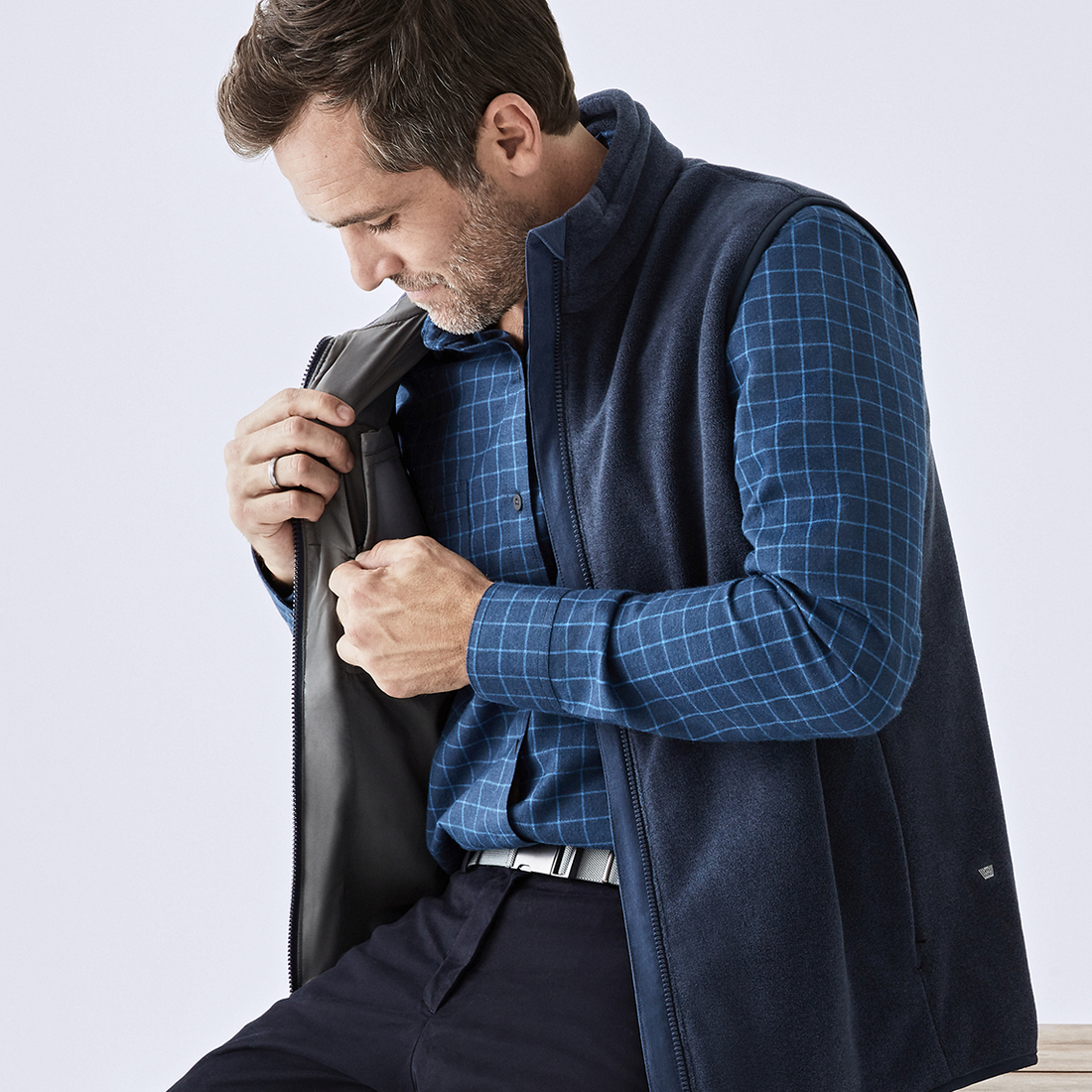 Image of a man wearing a WARMKNIT button up and zips up a pocket on the inside of his vest