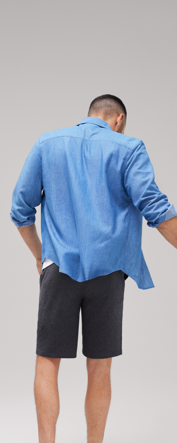 Back image of a man wearing a blue long sleeve button up and grey shorts